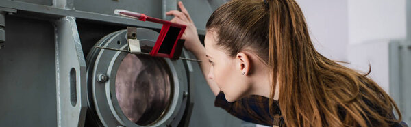 Вид сбоку брюнетки сварщика глядя на вакуумную лазерную сварочную машину на заводе, баннер 