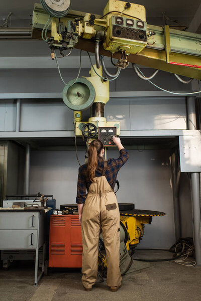 Back view of welder in overalls and shirt working on welding machine in factory 
