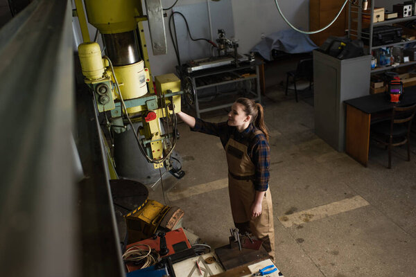 High angle view of smiling welder working with welding machine in factory 