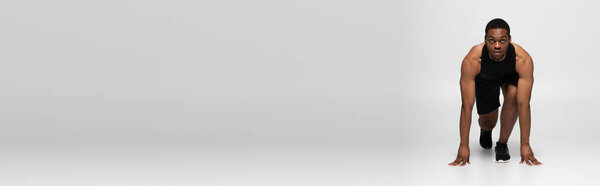 full length of african american sportsman in starting pose before running on grey, banner