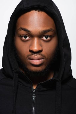 Kapüşonlu genç Afrikalı Amerikalı adam gri kameraya bakıyor.