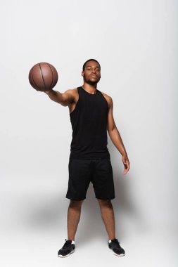 Tam boy Afrika kökenli Amerikalı oyuncu elini griye uzatmış basketbol topunu tutuyor.