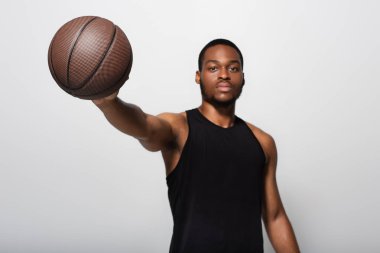 Genç Afrikalı Amerikalı, elini uzatıp basketbol topunu tutuyordu. Gri alanda izole edilmişti.