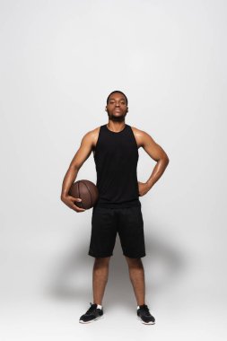 Tam boy Afro-Amerikan oyuncu elini griye koyup basketbol topunu tutuyor.