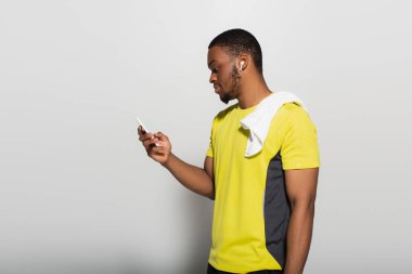 Kulağında kulaklık olan Afro-Amerikan sporcusunun gri üzerinde akıllı telefon kullanışının yan görüntüsü