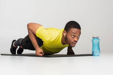 Sportif Afro-Amerikalı kulaklıklı bir adam spor minderinin yanında şınav çekiyor.
