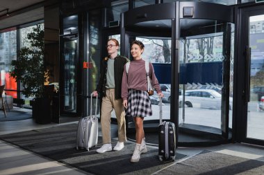 Bavulları olan genç bir çift otel lobisinde yürüyor. 