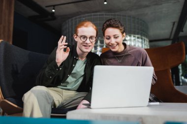 Genç gülümseyen turistler otel lobisindeki bulanık laptopta görüntülü arama yapıyorlar. 