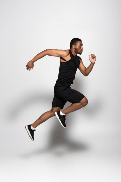 full length of african american sportsman levitating while running on grey 