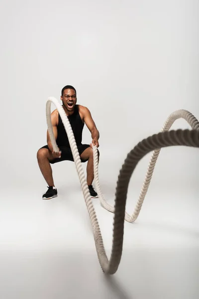 Full Length African American Sportsman Screaming While Exercising Battle Ropes — Stock Photo, Image