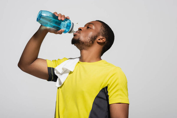 african american sportsman drinking water from sports bottle isolated on grey