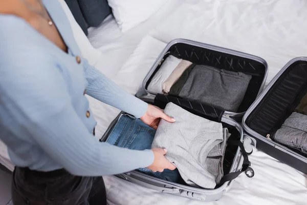 ホテルのベッドでスーツケースから服を取る若い女性の作物ビュー — ストック写真