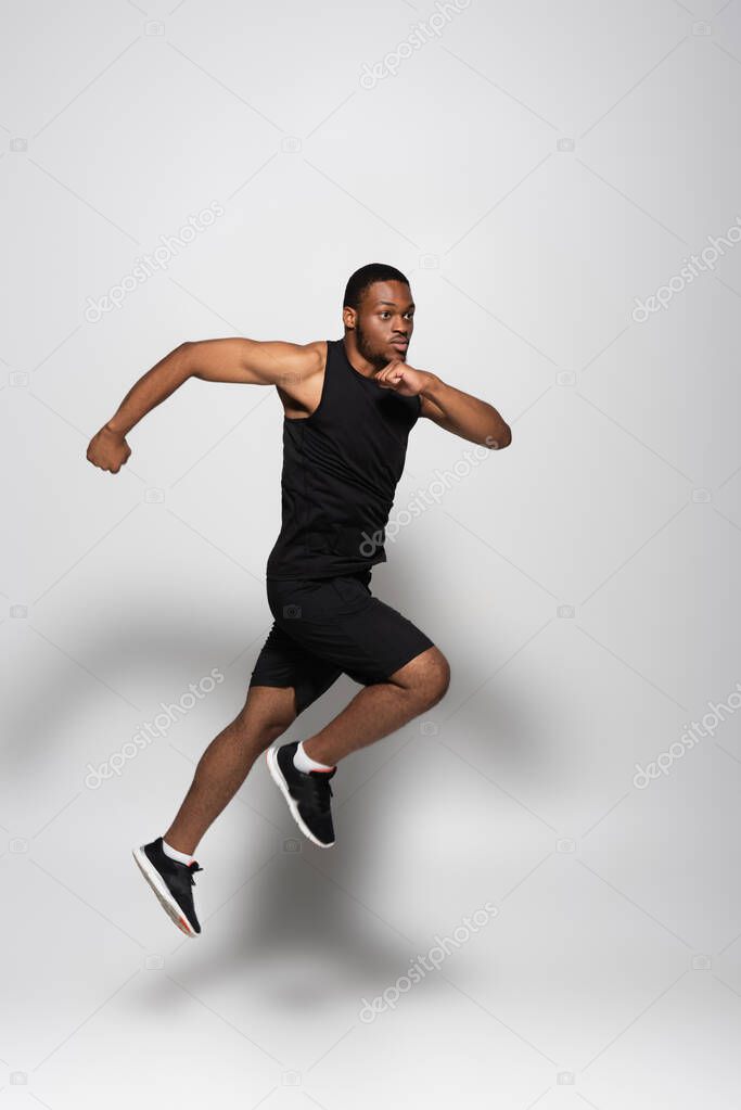 full length of fast african american sportsman levitating while running on grey 