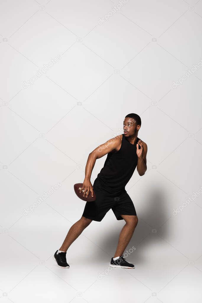 full length of african american sportsman playing rugby and running away on grey 