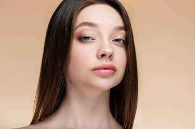 Esmer genç kadın bej renkli kameraya bakıyor. 