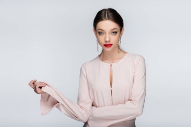 Gri renkte poz verirken kırmızı dudaklı genç kadın kameraya bakıyor.