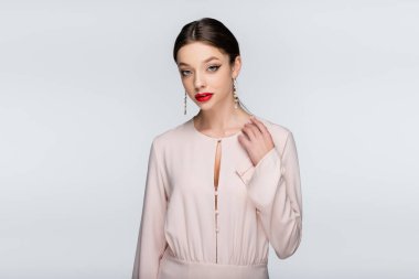 Küpeli genç bir kadın. Kırmızı dudaklı. Gri renkli kameraya bakıyor.