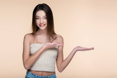 Genç ve neşe saçan kadın bej rengi elbisesiyle işaret ediyor. 
