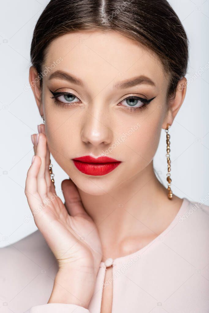 pretty woman in earrings with red lips looking at camera isolated on grey