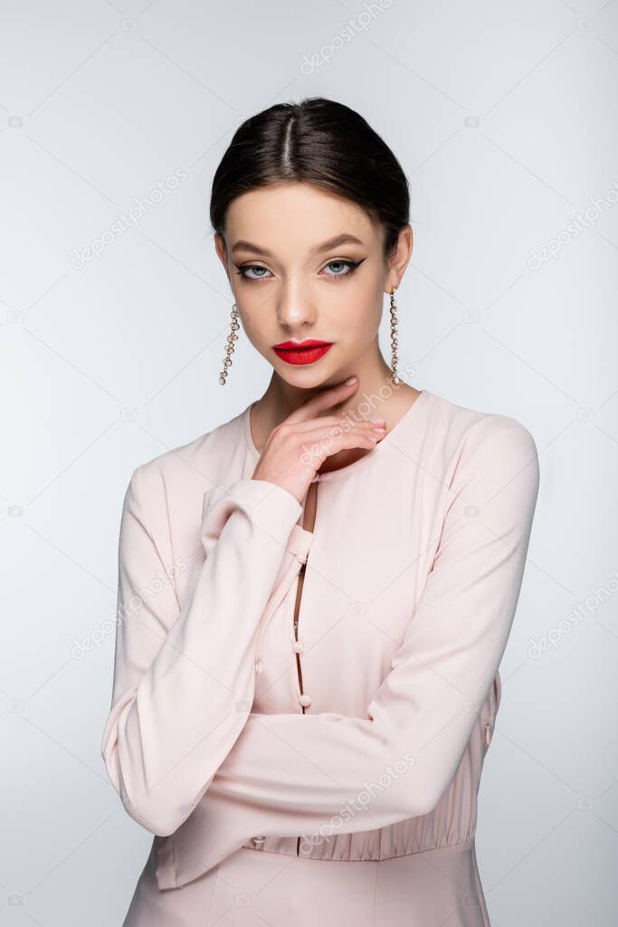 young woman in earrings and blouse looking at camera while posing isolated on grey