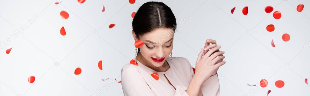 young and happy woman near falling rose petals on grey, banner
