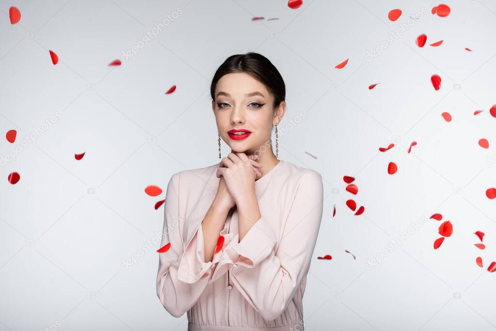 young and sensual woman with bright makeup near falling rose petals on grey