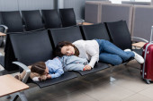 exhausted mother and daughter sleeping on airport seats in departure hall 