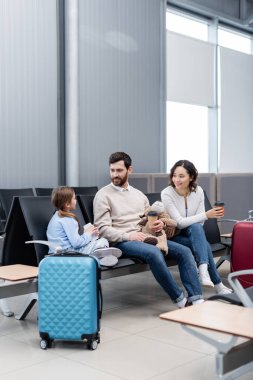 Mutlu ebeveynler havaalanında akıllı telefonlu kızlarına bakıyor. 