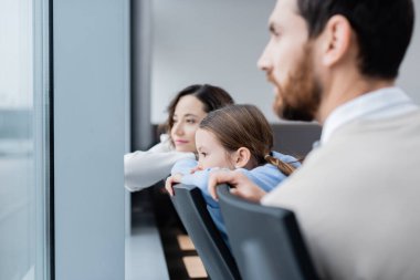 Bulanık ebeveynlerin yanındaki havaalanı penceresine bakan hayalperest çocuk. 