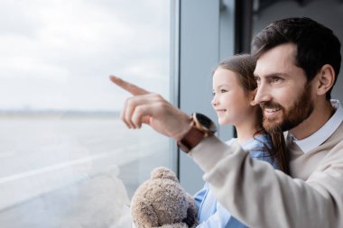 Mutlu baba, havaalanındaki neşeli kızın yanındaki pencereyi işaret ediyor. 