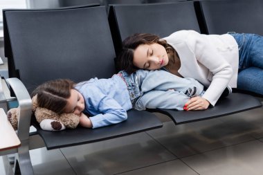 Anne ve kızı kalkış salonundaki havaalanı koltuklarında uyuyorlar. 