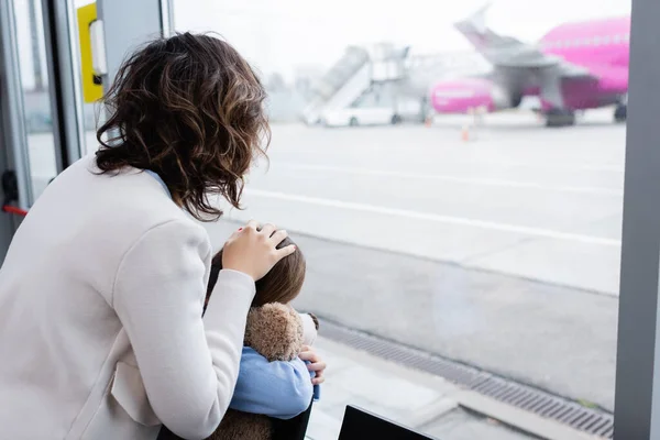空港の窓の後ろの飛行機を見ている母親と娘の姿を — ストック写真