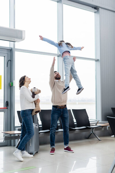 cheerful father lifting daughter near wife in airport lounge 