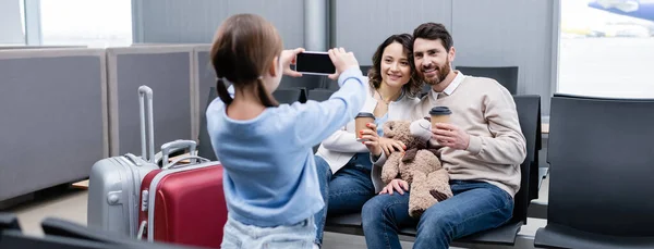 空港ラウンジバナーの紙コップで幸せな両親の写真を撮る女の子 — ストック写真