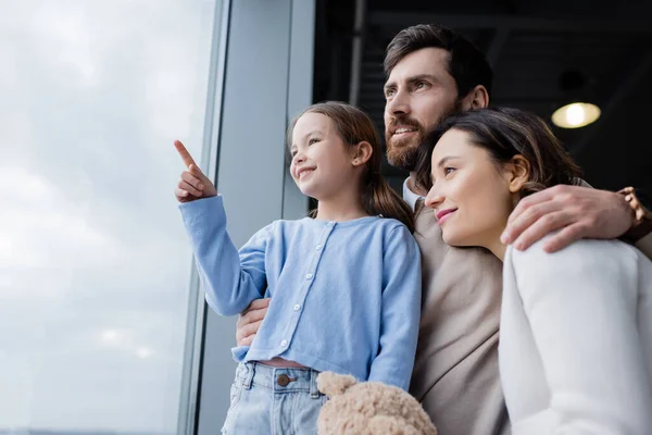 Happy Girl Pointing Finger Window Cheerful Parents Airport — Stock Fotó