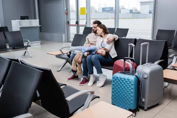 girl sleeping on knees of tired parents in airport lounge