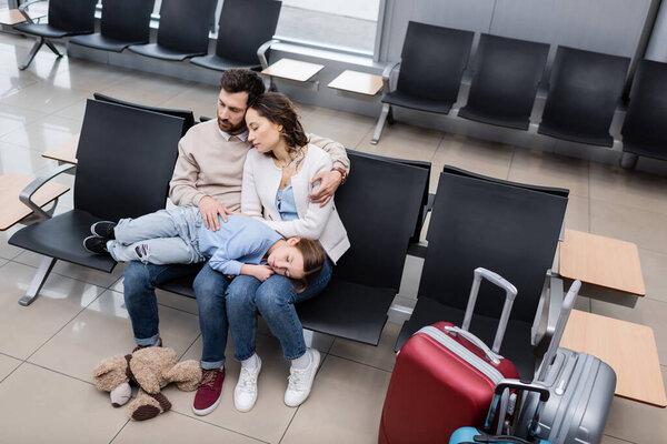high angle view of girl sleeping on knees of tired parents in airport lounge 