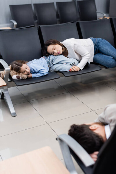 mother and daughter sleeping on airport seats near blurred man in departure hall 