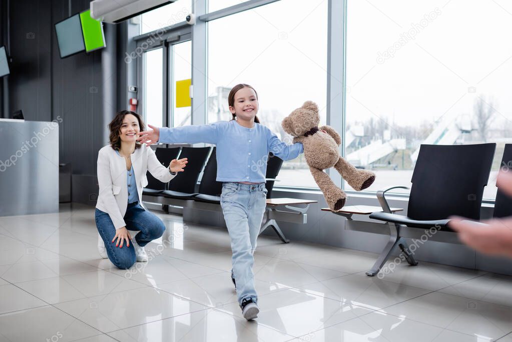 happy kid with teddy bear welcoming blurred father in airport 