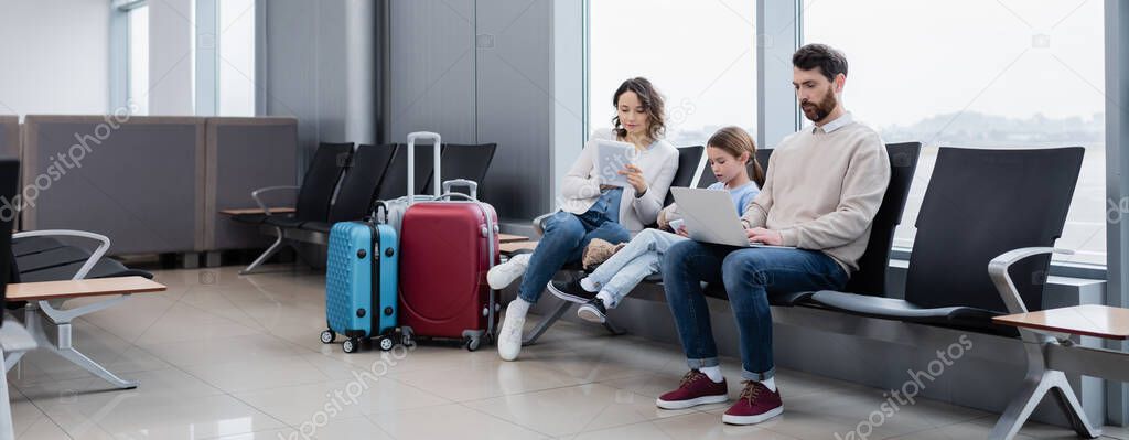 family using devices while sitting in airport lounge, banner