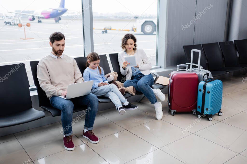 family using devices while sitting near luggage in airport lounge 