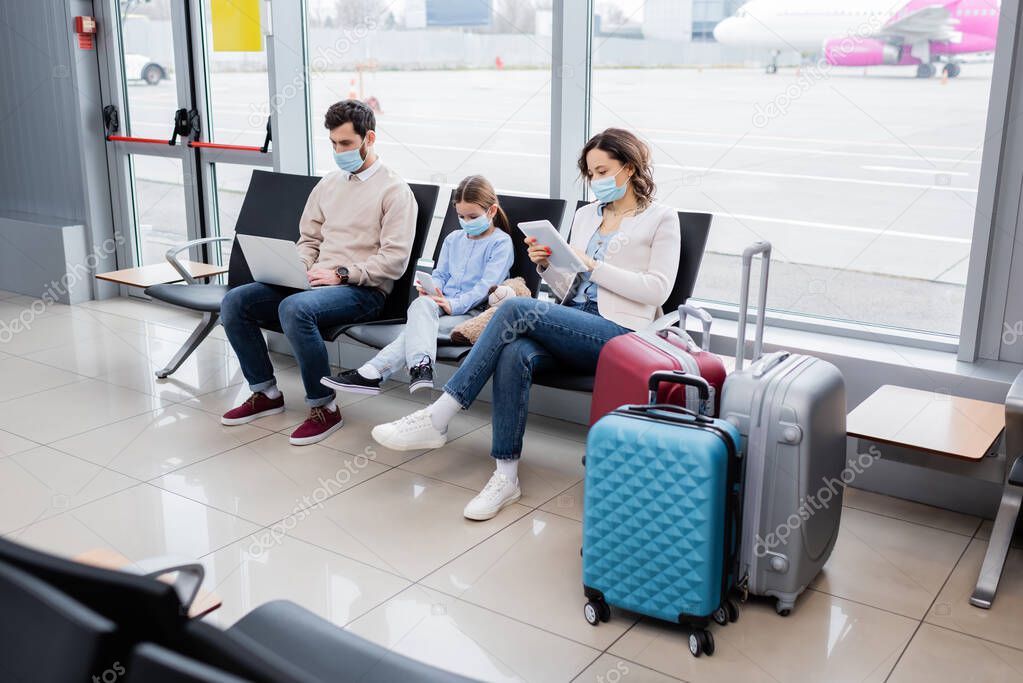 parents and kid in medical masks using gadgets in airport