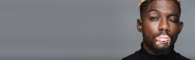 portrait of young african american man with vitiligo and one closed eye looking at camera isolated on grey, banner