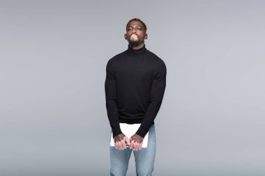 young african american man with vitiligo and stylish hairstyle standing with laptop isolated on grey
