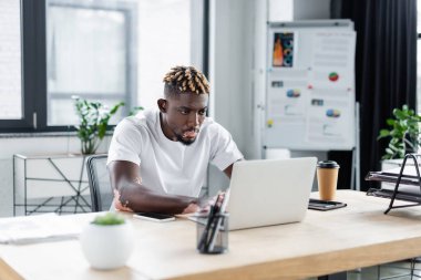 young african american man with vitiligo working on laptop near paper cup in office