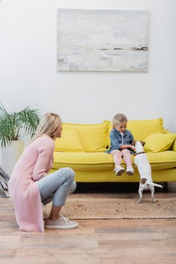 Child playing with jack russell terrier on couch near mom at home