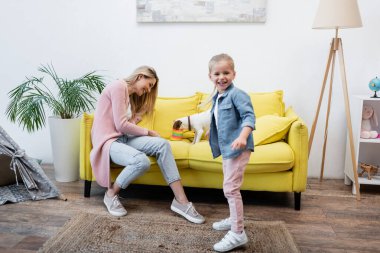 Smiling girl looking at camera near mom and jack russell terrier at home 