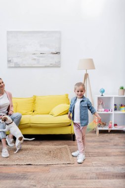 Smiling girl holding slinky near mom and jack russell terrier at home 