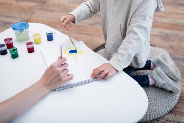 Cropped view of mom and child drawing on sketchbook at home 
