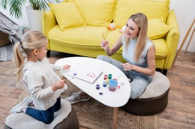 High angle view of positive parent holding paintbrush near daughter and sketchbook at home 